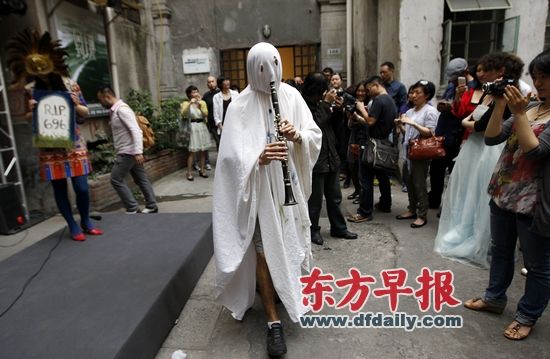 一位艺术家身披白衣，头上包着白布吹奏乐器，引来众多围观者。 早报记者 赵昀 图