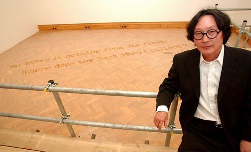 徐冰站在他的作品前，地板上显示出“As there is nothing from the first，Where Does the Dust Itself Collect?”（本来无一物，何处惹尘埃？）
