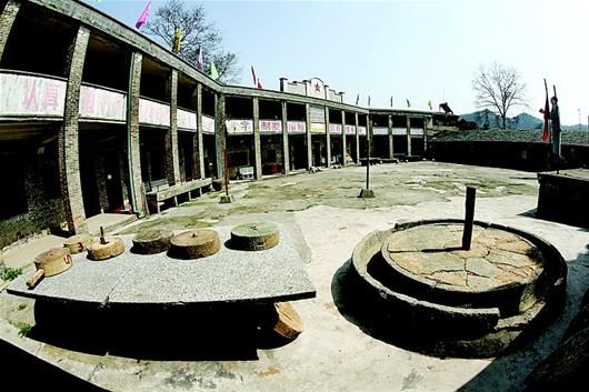 图为：博物馆建在一座废弃的小学里，墙上的标语有一段写的是毛主席语录，院内一角陈列着各式各样的石磨。