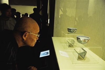 观众正在看展台上摆放的清道光斗彩荷塘鸳鸯纹墩式碗和与之对比的赝品（图中有缺口的）。实习生 刘梦 摄
