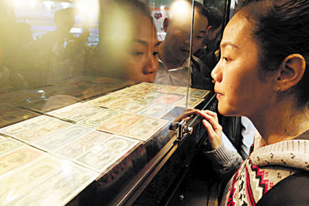 图为金融博览会展出的第一套人民币吸引住了一位参观者的目光。